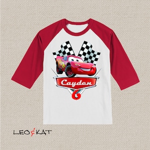 Może przedstawiać: Czerwono-biała koszulka bejsbolowa z czerwonym samochodem wyścigowym i szachownicą. Koszulka ma napis "Cayden" i numer "6".