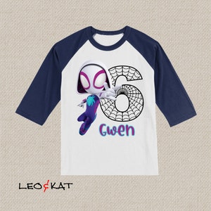 May include: White and navy blue raglan shirt featuring a cartoon image of Spider-Gwen with the number 6 and the name "Gwen". The shirt has three-quarter sleeves and a colourful design.