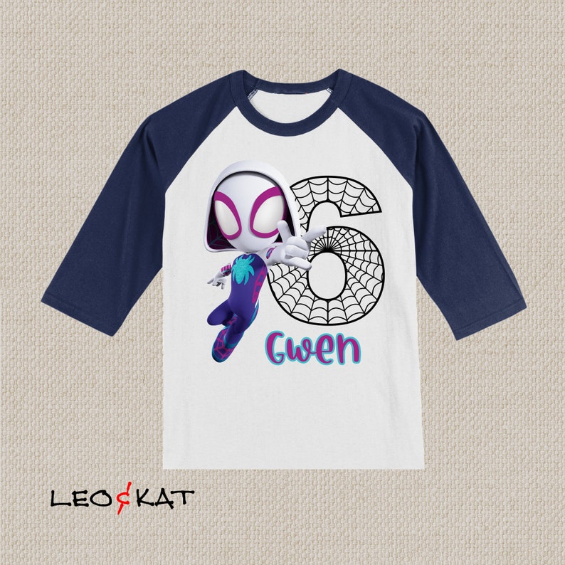 May include: White and navy blue raglan shirt featuring a cartoon image of Spider-Gwen with the number 6 and the name "Gwen". The shirt has three-quarter sleeves and a colourful design.