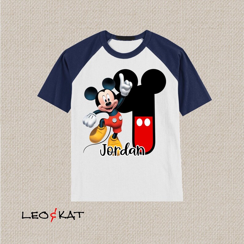 Peut inclure: T-shirt &agrave; manches raglan blanche et bleu marine avec un motif Mickey Mouse et le nom "Jordan" imprim&eacute; sur le devant.