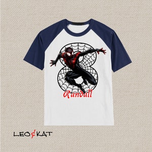 Puede incluir: Camiseta de manga raglan blanca y azul marino con un personaje de Spiderman negro y rojo en un dise&ntilde;o de telara&ntilde;a. La camiseta tiene el nombre "Randall" impreso en ella.