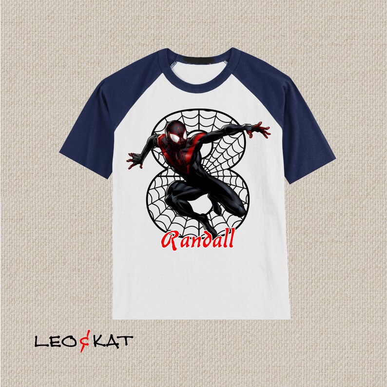Puede incluir: Camiseta de manga raglan blanca y azul marino con un personaje de Spiderman negro y rojo en un dise&ntilde;o de telara&ntilde;a. La camiseta tiene el nombre "Randall" impreso en ella.