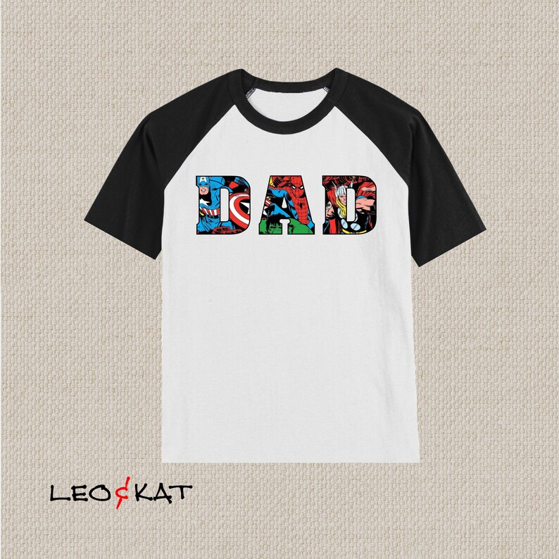 Op de afbeelding: Wit en zwart baseballshirt met een afbeelding van het woord "DAD" gemaakt van stripfiguren.