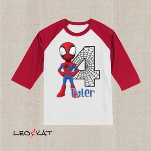 May include: A white and red baseball tee shirt with a red and blue Spiderman character and a black number 4 with a spiderweb design. The name Tyler is written in blue below the number.