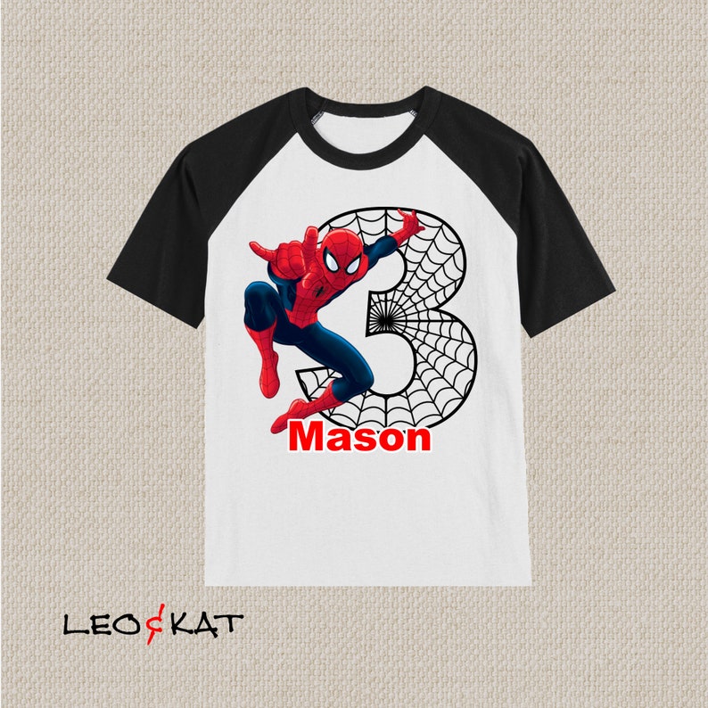 Puede incluir: Una camiseta blanca y negra de manga raglan con un gr&aacute;fico de Spiderman rojo y azul y el n&uacute;mero 3. El gr&aacute;fico tambi&eacute;n incluye una telara&ntilde;a negra. El nombre "Mason" est&aacute; escrito en rojo debajo del gr&aacute;fico.