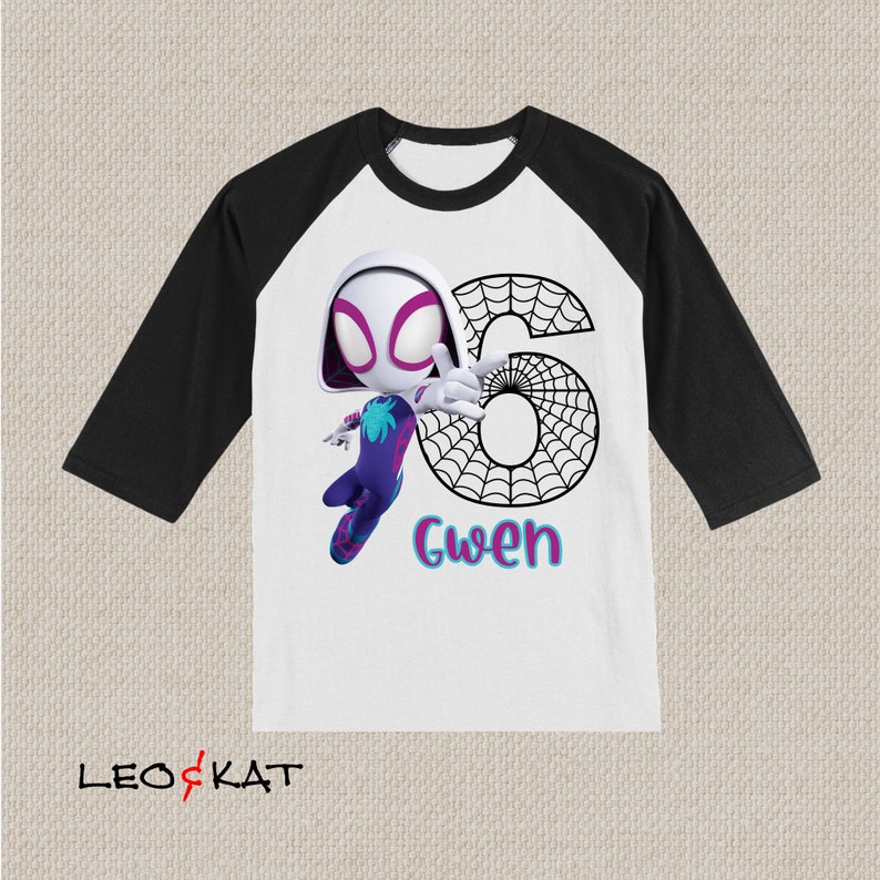 May include: A white and black raglan-style t-shirt with a cartoon Spider-Gwen illustration, the number 6, and the name "Gwen". The sleeves are black, and the body is white. The Spider-Gwen character is depicted in a dynamic pose, with a web design.