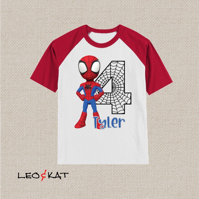 May include: White and red raglan t-shirt with a cartoon image of Spiderman, a black web design, and the number 4. The name Tyler is written below the number.