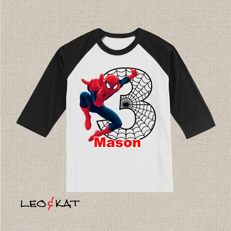 Puede incluir: Una camiseta de b&eacute;isbol blanca y negra con un gr&aacute;fico de Spiderman rojo y azul. El n&uacute;mero 3 est&aacute; en el fondo con un dise&ntilde;o de telara&ntilde;a negra. El nombre Mason est&aacute; escrito en rojo debajo del gr&aacute;fico.