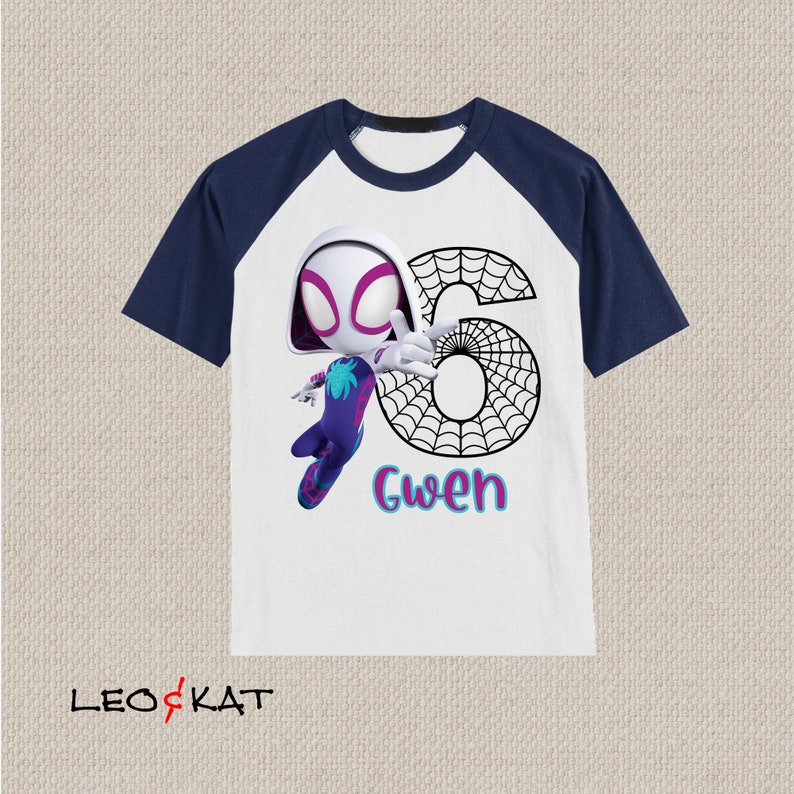 May include: White and navy blue raglan t-shirt featuring a cartoon illustration of Spider-Gwen with the number 6 and the name "Gwen". The graphic is in vibrant colours, with a spider web design incorporated into the number.