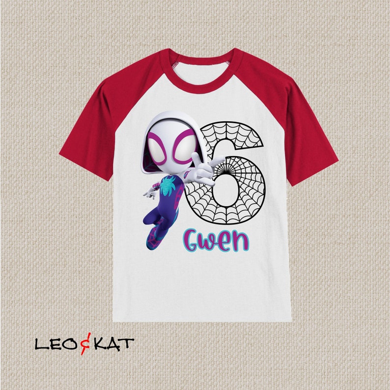 May include: White and red raglan t-shirt featuring a cartoon illustration of Spider-Gwen with the number 6 and the name "Gwen". The design includes a spider web and the character in a dynamic pose.
