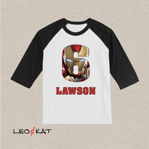 Pu&ograve; includere: Maglietta da baseball bianca e nera con un numero sei rosso che presenta il volto di Iron Man. Il nome Lawson &egrave; stampato in rosso sotto il numero.