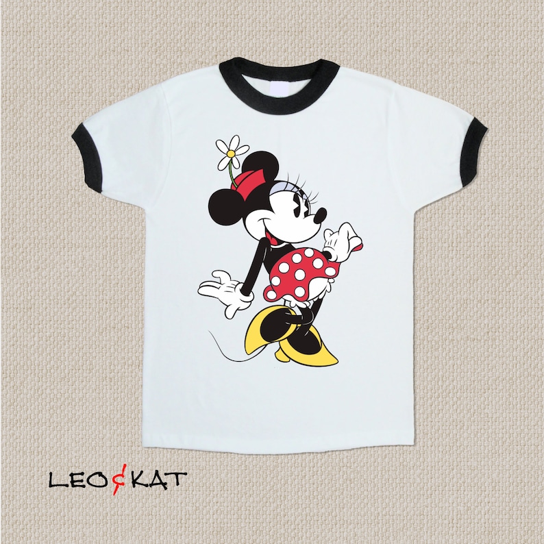 K&ouml;nnte beinhalten: Wei&szlig;es T-Shirt mit schwarzem Ringelkragen und schwarzen &Auml;rmeln. Das Shirt zeigt ein Cartoon-Bild von Minnie Mouse, die ein rotes Kleid mit wei&szlig;en Punkten und einer roten Schleife tr&auml;gt.