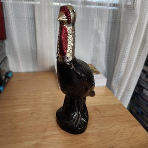 May include: A black glass turkey-shaped bottle with a red and silver top. The bottle is sitting on a wooden surface.