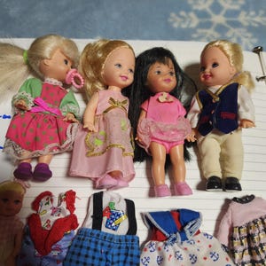 May include: A collection of small dolls with various outfits. The dolls have blonde, black, and light brown hair. The outfits include dresses, tops, and pants in pink, blue, and white. Some dolls have pacifiers.