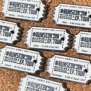 Könnte beinhalten: Eine Sammlung von silberfarbenen, weißen Konzertkarten-Anstecknadeln. Jede Anstecknadel zeigt den Text "#RUNSEOKJIN EP. TOUR" zusammen mit einer Stadt und einem Datum, wie "Goyang 28.-29. Juni 2025". Die Anstecknadeln sind auf einer Pinnwand angeordnet.