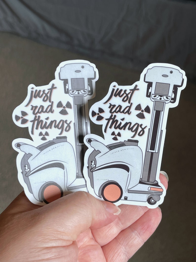 May include: Two white and gray robot stickers with the text "just rad things" and a radioactive symbol. The robots have orange wheels and are holding a small, gray object.