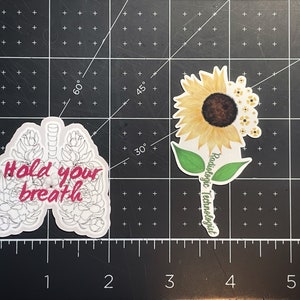 May include: Two stickers, one with a white outline of lungs with pink flowers and the text "Hold your breath", and the other with a yellow sunflower and the text "Radiologic Technologist".
