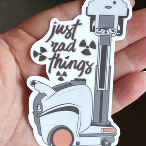 May include: White sticker with a black and white illustration of a robot with the text "just rad things" and a radioactive symbol.