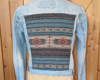 May include: A light blue denim jacket with a colorful patterned fabric patch on the back. The patch features geometric designs in shades of blue, brown, and red.