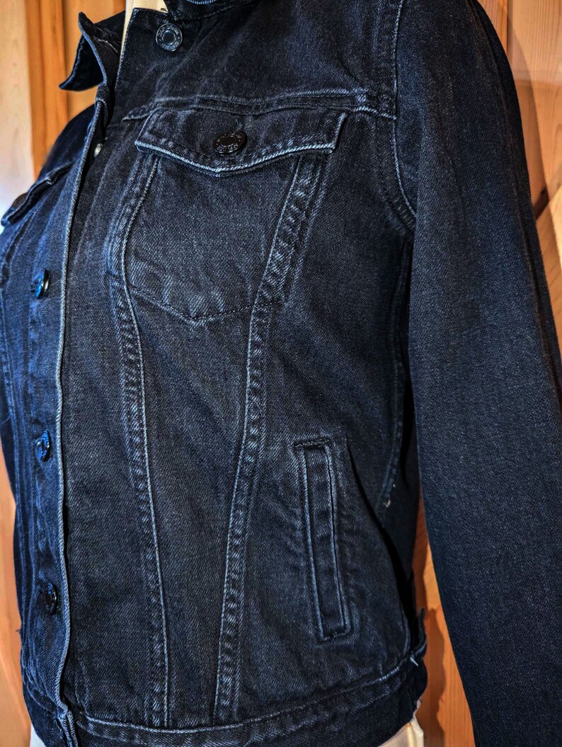 May include: A dark blue denim jacket with a button closure and multiple pockets.