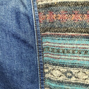 May include: Close-up of a denim fabric with a contrasting woven fabric panel. The denim is blue and the woven fabric is a mix of brown, white, and blue.