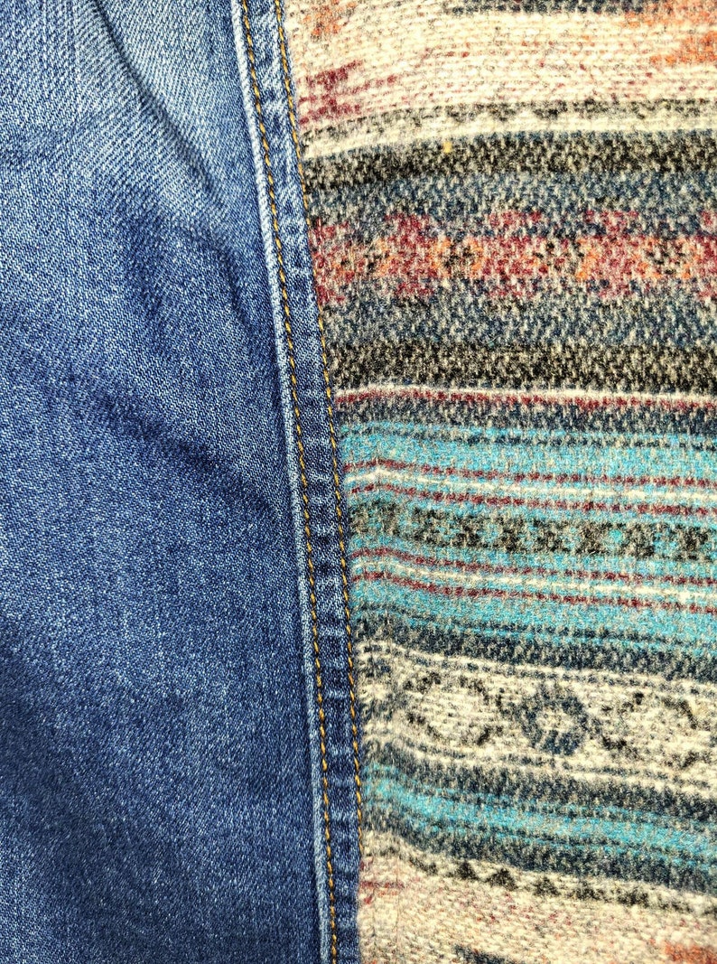 May include: Close-up of a denim fabric with a contrasting woven fabric panel. The denim is blue and the woven fabric is a mix of brown, white, and blue.