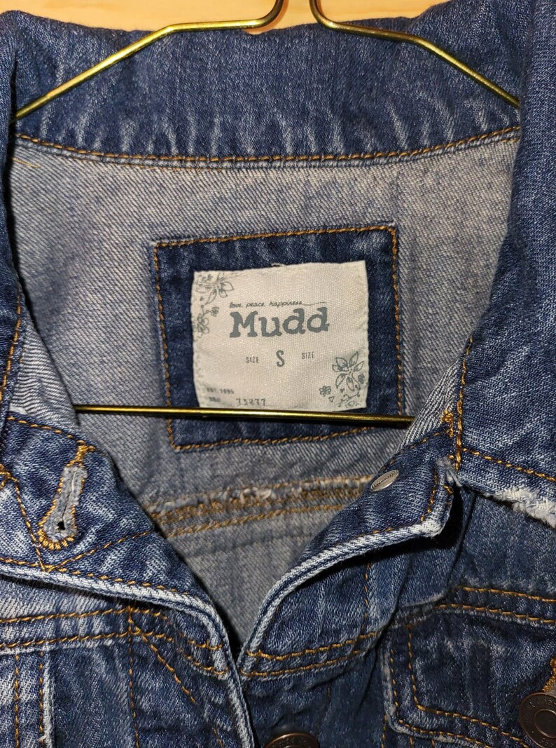 May include: A blue denim jacket with a label that reads "Mudd" and "Size S".