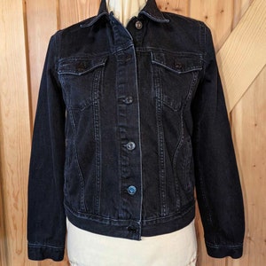 May include: A black denim jacket with a button closure and two front pockets.