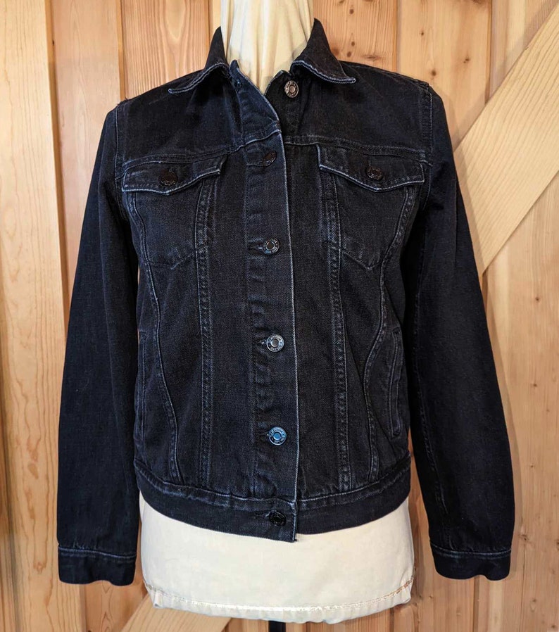 May include: A black denim jacket with a button closure and two front pockets.