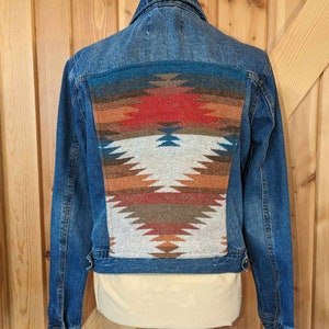 May include: A blue denim jacket with a colorful geometric pattern on the back. The pattern is in shades of red, orange, brown, and white.
