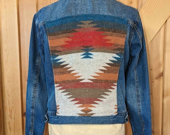 May include: A blue denim jacket with a colorful geometric pattern on the back. The pattern is in shades of red, orange, brown, and white.