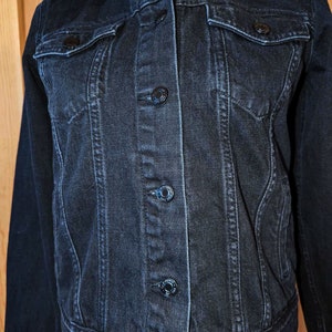 May include: A dark blue denim jacket with a classic style. The jacket has a button-up front, two chest pockets, and long sleeves.