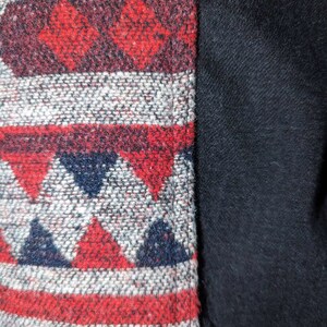 May include: Close-up of a woven fabric with a geometric pattern in shades of red, white, and blue. The fabric is sewn to a solid black fabric.