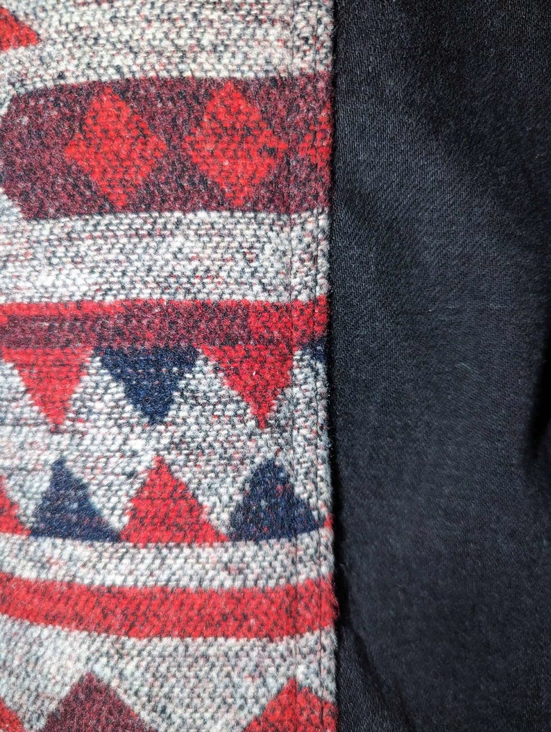 May include: Close-up of a woven fabric with a geometric pattern in shades of red, white, and blue. The fabric is sewn to a solid black fabric.