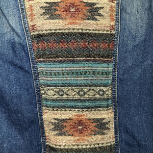 May include: A blue denim jacket with a colorful woven patch on the back. The patch features geometric patterns in shades of blue, brown, and red.