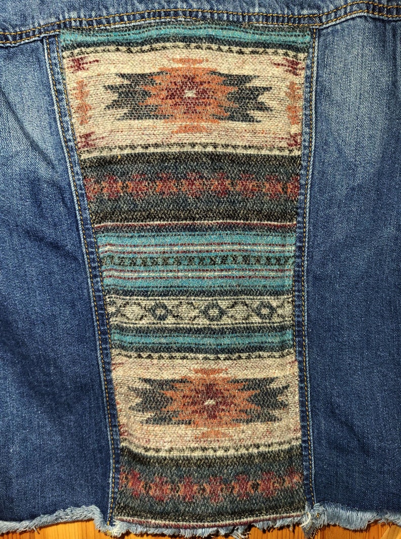 May include: A blue denim jacket with a colorful woven patch on the back. The patch features geometric patterns in shades of blue, brown, and red.