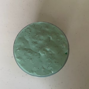 May include: A close-up of a light green slime with black flecks in a clear container.