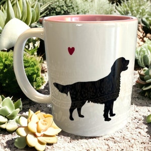 Könnte beinhalten: Weiße Keramik-Kaffeetasse mit rosafarbenem Rand. Die Tasse zeigt eine schwarze Silhouette eines Hundes mit einem roten Herzen darüber.