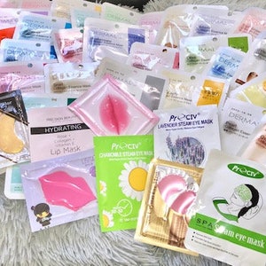 May include: An assortment of face and eye masks in various colours and designs. The masks are packaged in individual pouches and feature different ingredients and benefits, such as green tea, lavender, and collagen. The text on the packaging includes "Dermal", "Preciv", "Hydrating Lip Mask", "Lavender Steam Eye Mask", "Charcoal Steam Eye Mask", and "Spa Steam Eye Mask".