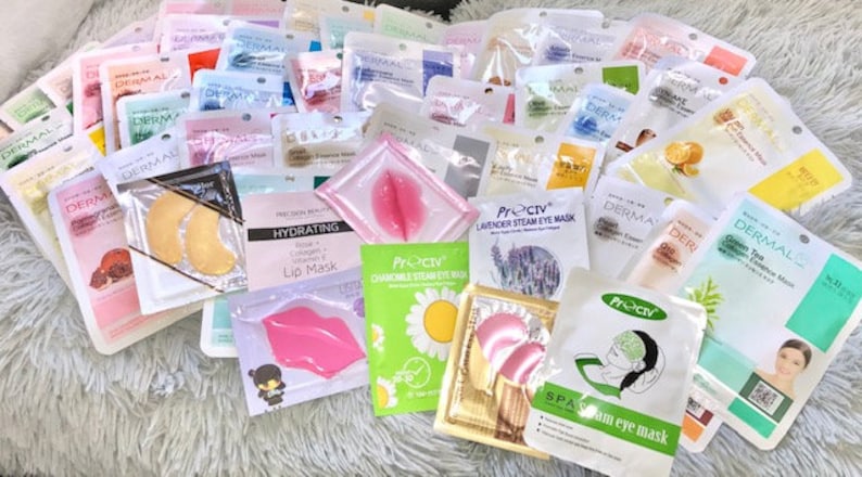 May include: An assortment of face and eye masks in various colours and designs. The masks are packaged in individual pouches and feature different ingredients and benefits, such as green tea, lavender, and collagen. The text on the packaging includes "Dermal", "Preciv", "Hydrating Lip Mask", "Lavender Steam Eye Mask", "Charcoal Steam Eye Mask", and "Spa Steam Eye Mask".
