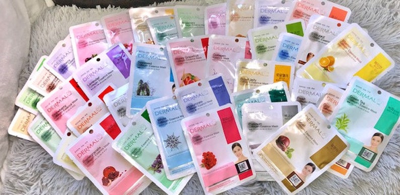 May include: A selection of face masks in individual sachets, featuring various ingredients and benefits. The sachets are white with blue and green accents, and the text 'Dermal' is printed on each sachet.