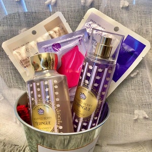 May include: A silver metal basket filled with bath and body products. The basket contains two bottles of whipped berry meringue body lotion, a bottle of whipped berry meringue body spray, and a pink face mask.