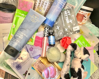 May include: A collection of bath and body products, including lotions, bath bombs, and shower gels. There are also several face masks, a headband, and a small bottle of essential oil. The products are arranged on a fluffy white surface.