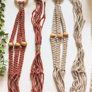 May include: Three macrame plant hangers with wooden beads. The hangers are made with natural fibers in shades of brown, beige, and rust.