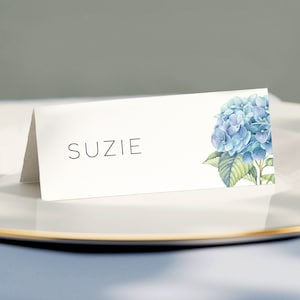 A folded wedding name card on textured premium paper with a blue hydrangea print. The font is thin and spaced evenly reflect the elegance of the wedding theme.