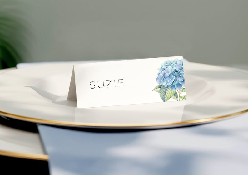 A folded wedding name card on textured premium paper with a blue hydrangea print. The font is thin and spaced evenly reflect the elegance of the wedding theme.