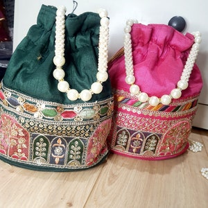 Puede incluir: Dos bolsas de cord&oacute;n con asas de perlas. Una bolsa es verde con bordados dorados y la otra es rosa con bordados dorados.