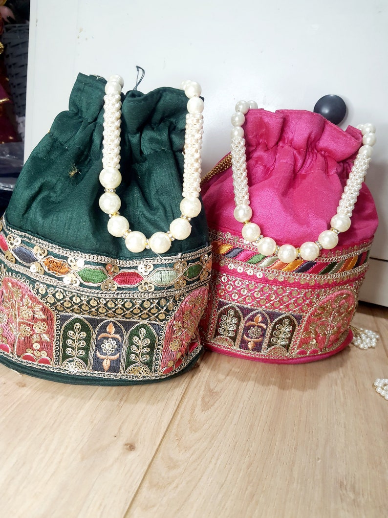Puede incluir: Dos bolsas de cord&oacute;n con asas de perlas. Una bolsa es verde con bordados dorados y la otra es rosa con bordados dorados.