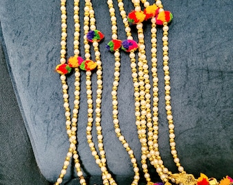 May include: A set of nine gold beaded strings with colorful pom-poms and bells at the ends. The strings are hanging from a blue fabric surface.