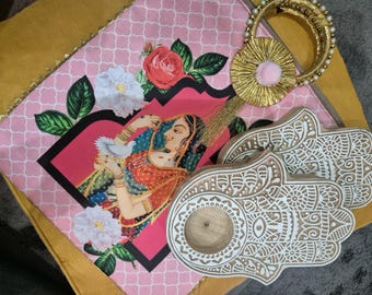 May include: A pink and gold fabric pouch with a floral design and a pair of white wooden hand-shaped incense holders.